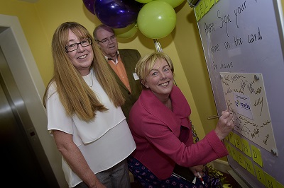Minister Regina Doherty signs her name to a commemorative card with Sharon Brennan, Coordinator of North Dublin MABS, Swords and Brian Lally, former Chairperson of Fingal MABS.