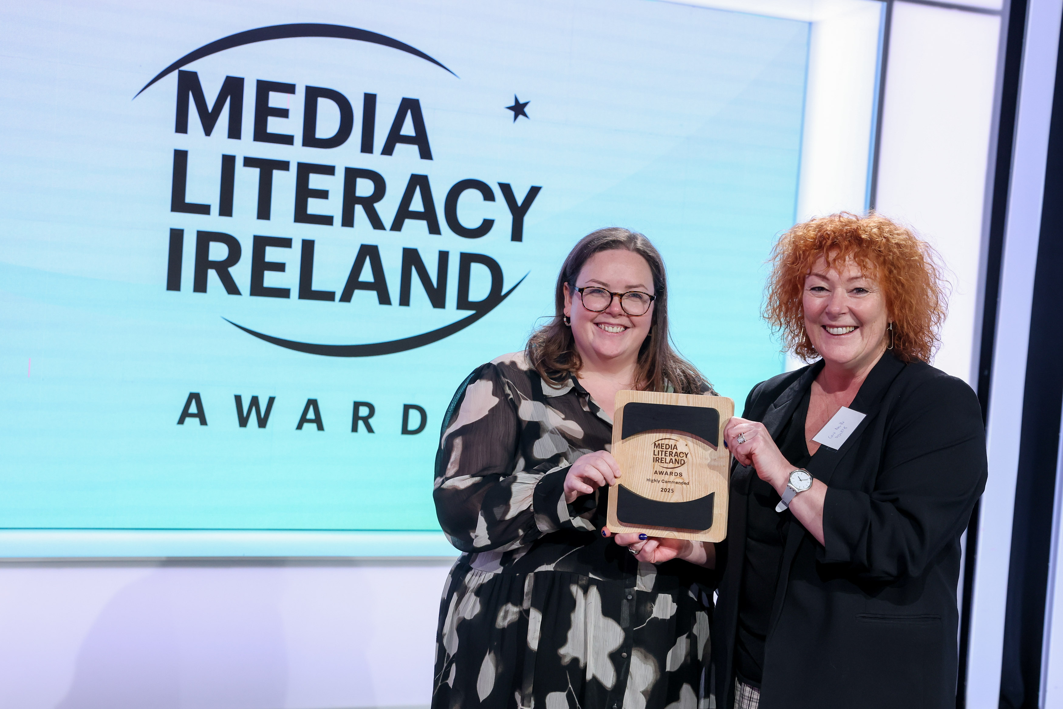 Two women standing in front of a screen which reads 'Media Literacy Ireland Awards'. They are holding an award in their hands.